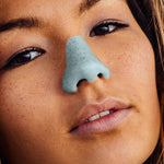 Load image into Gallery viewer, Young woman wearing blue Nöz sunscreen on her nose.

